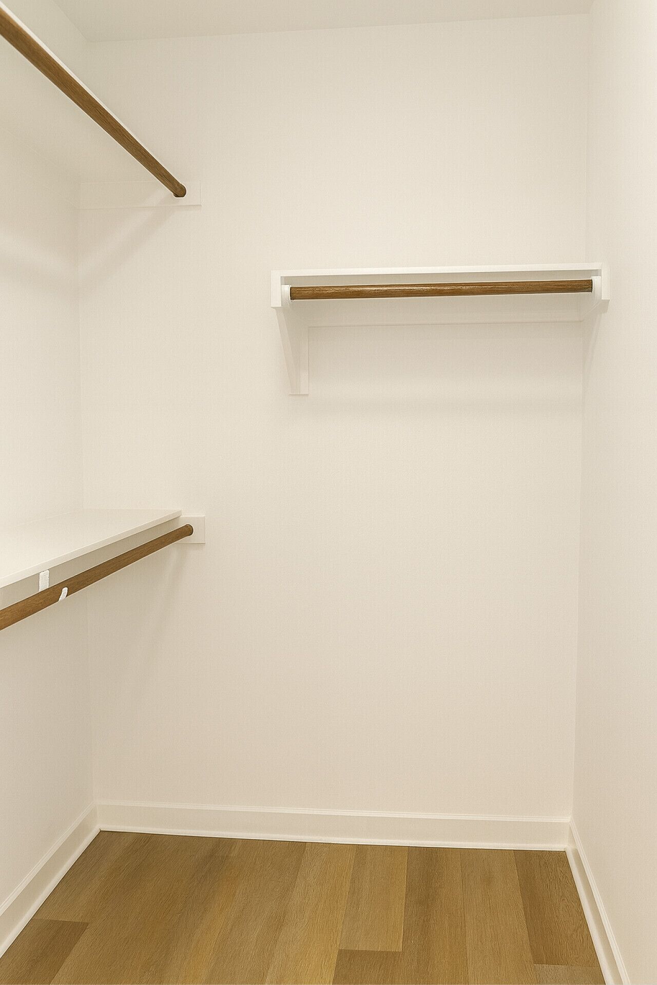 A room with white walls, wooden flooring, and three white shelves with wooden rods.