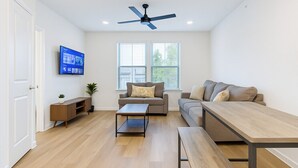 A modern living room with a sofa, a coffee table, a TV mounted on the wall, and a ceiling fan. - Cozy & Chic - Worker Friendly (Sherman)