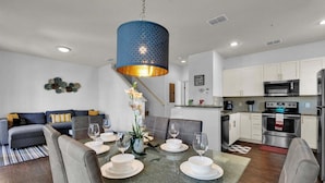 A modern kitchen with stainless steel appliances, a dining area with a glass table set for four, and a blue pendant light above the table. - Gdl3206 (Kissimmee)