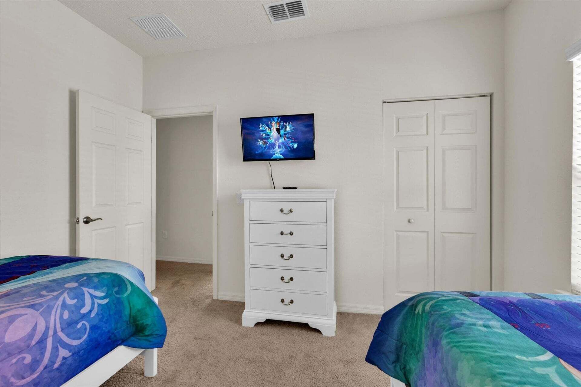 A bedroom with two beds, a dresser, a television, and a door.