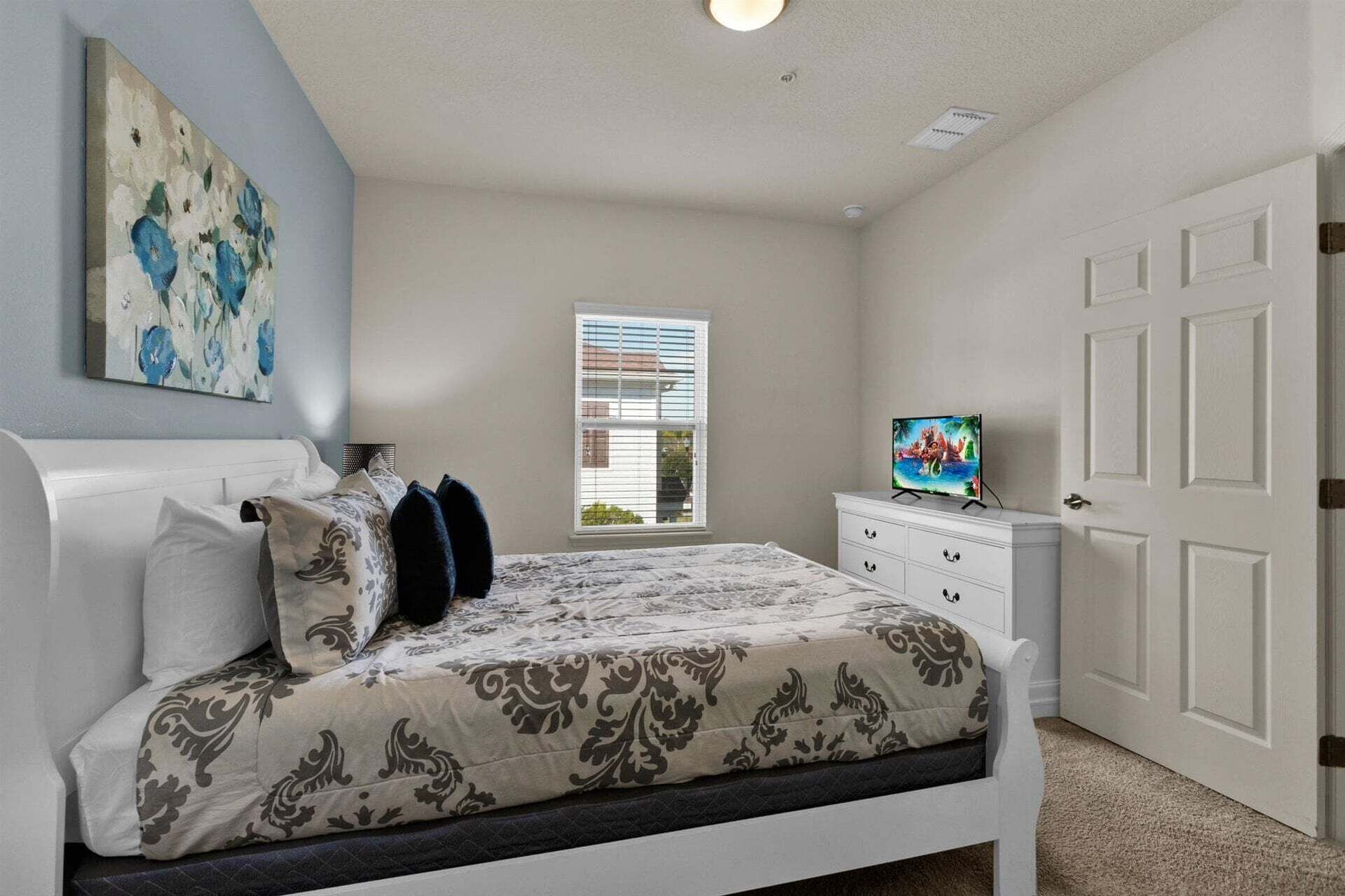 Un dormitorio con cama, cómoda, televisor y ventana con persianas.