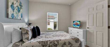 Un dormitorio con cama, cómoda, televisor y ventana con persianas.
