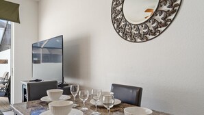 A dining area with a marble table, white plates, and wine glasses. There is a large mirror on the wall and a television on the left. - Op7678 Windsor Hills 3 Bedroom Private Pool Townhome (Kissimmee)