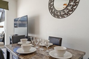 A dining area with a marble table, white plates, and wine glasses. There is a large mirror on the wall and a television on the left. - Op7678 Windsor Hills 3 Bedroom Private Pool Townhome (Kissimmee)