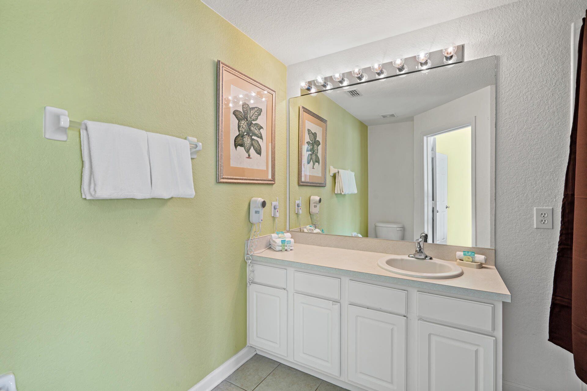 A bathroom with a vanity, sink, and mirror. There are towels hanging on the wall and a framed picture above the mirror.