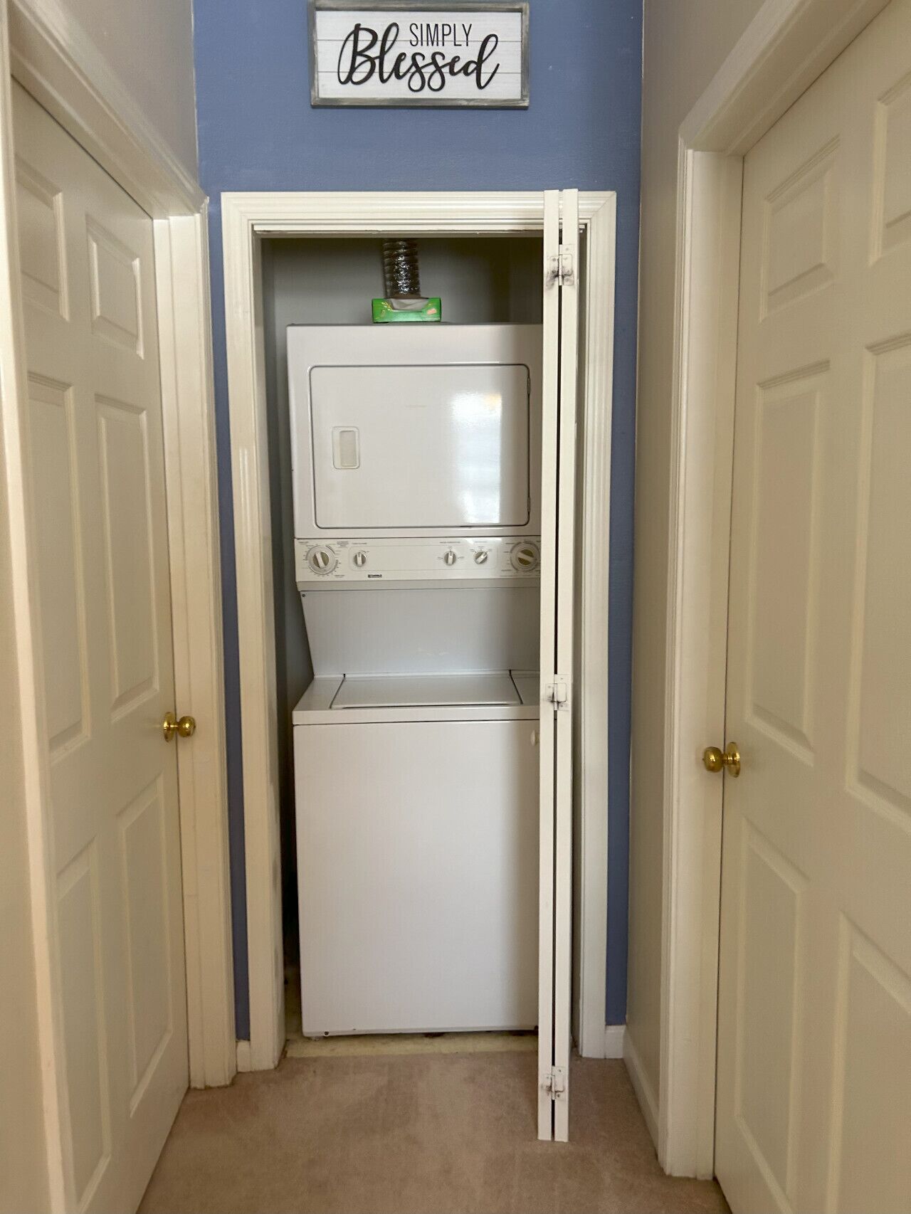 A laundry room with a washer and dryer, a sign above stating "SIMPLY Blessed," and a blue wall.