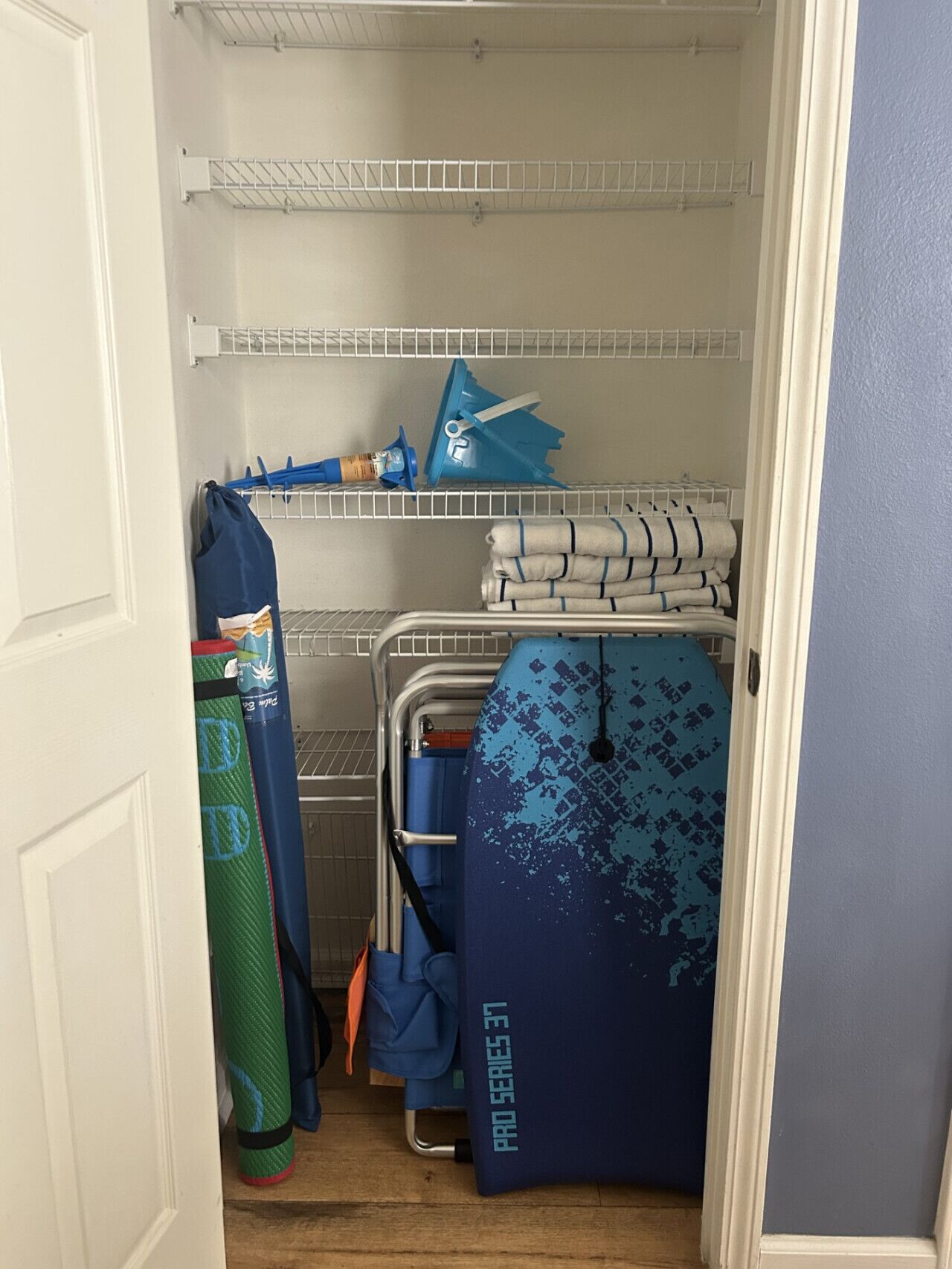 A storage closet with shelves, a blue folding chair, and a green mat.