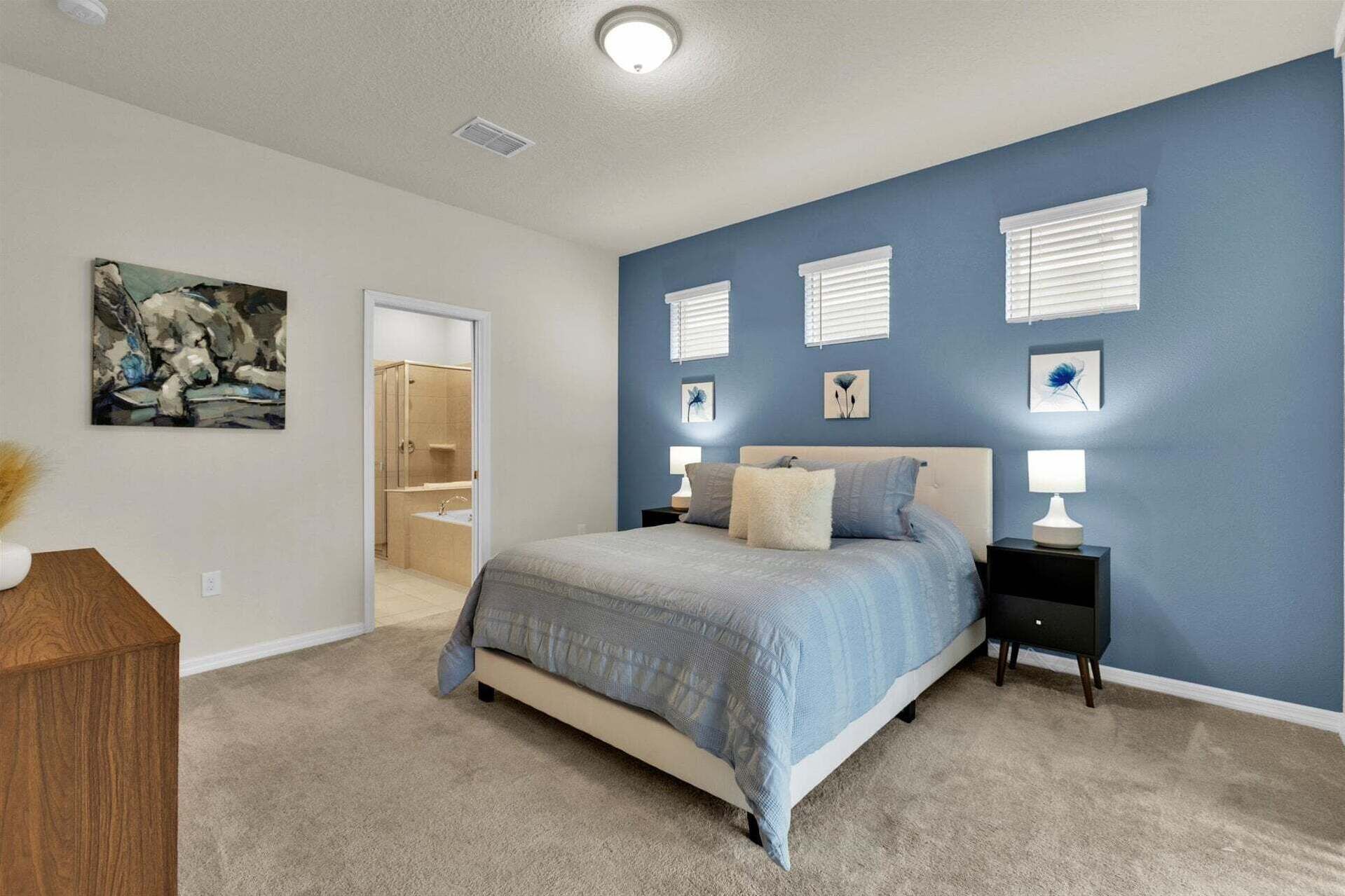 Une chambre à coucher avec un lit, des tables de chevet, une commode et une salle de bain visible à travers une porte ouverte.