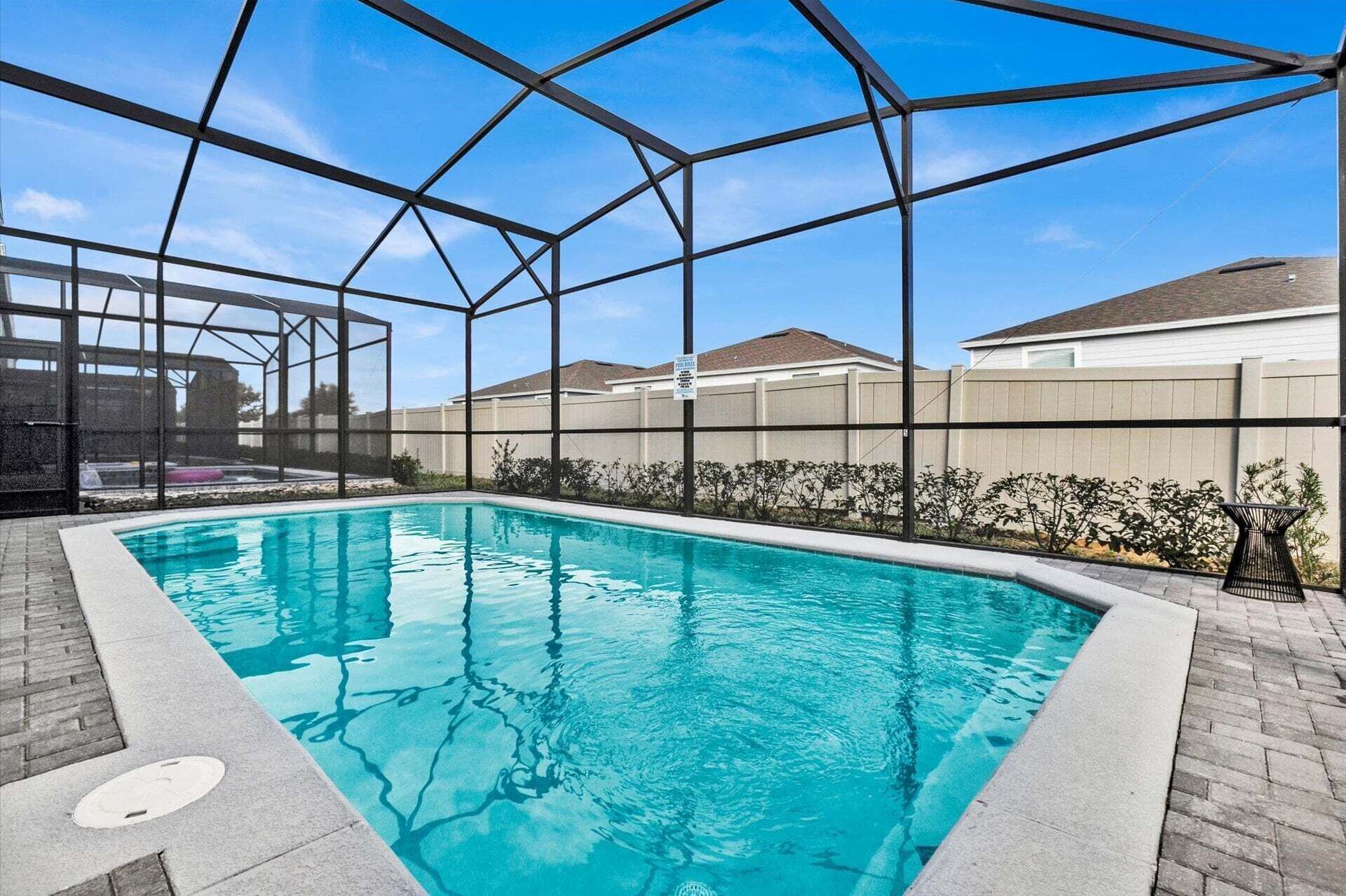 A swimming pool with a clear blue water, surrounded by a metal fence and a brick walkway.