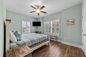 A bedroom with a bed, a ceiling fan, a TV, and two windows. - Chester St 115 (Myrtle Beach)