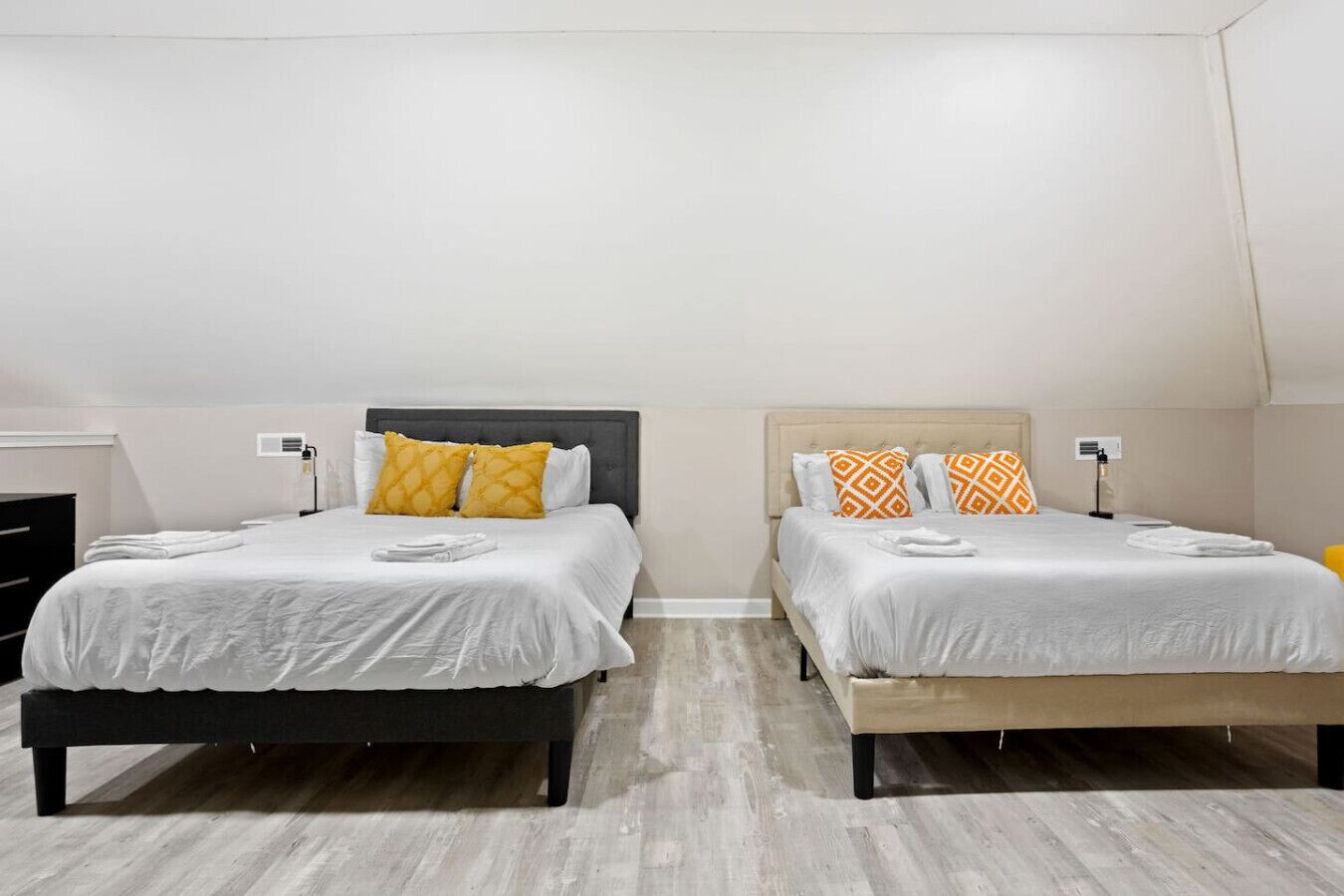Two twin beds with white bedding and patterned pillows, a wooden floor, and a white wall.