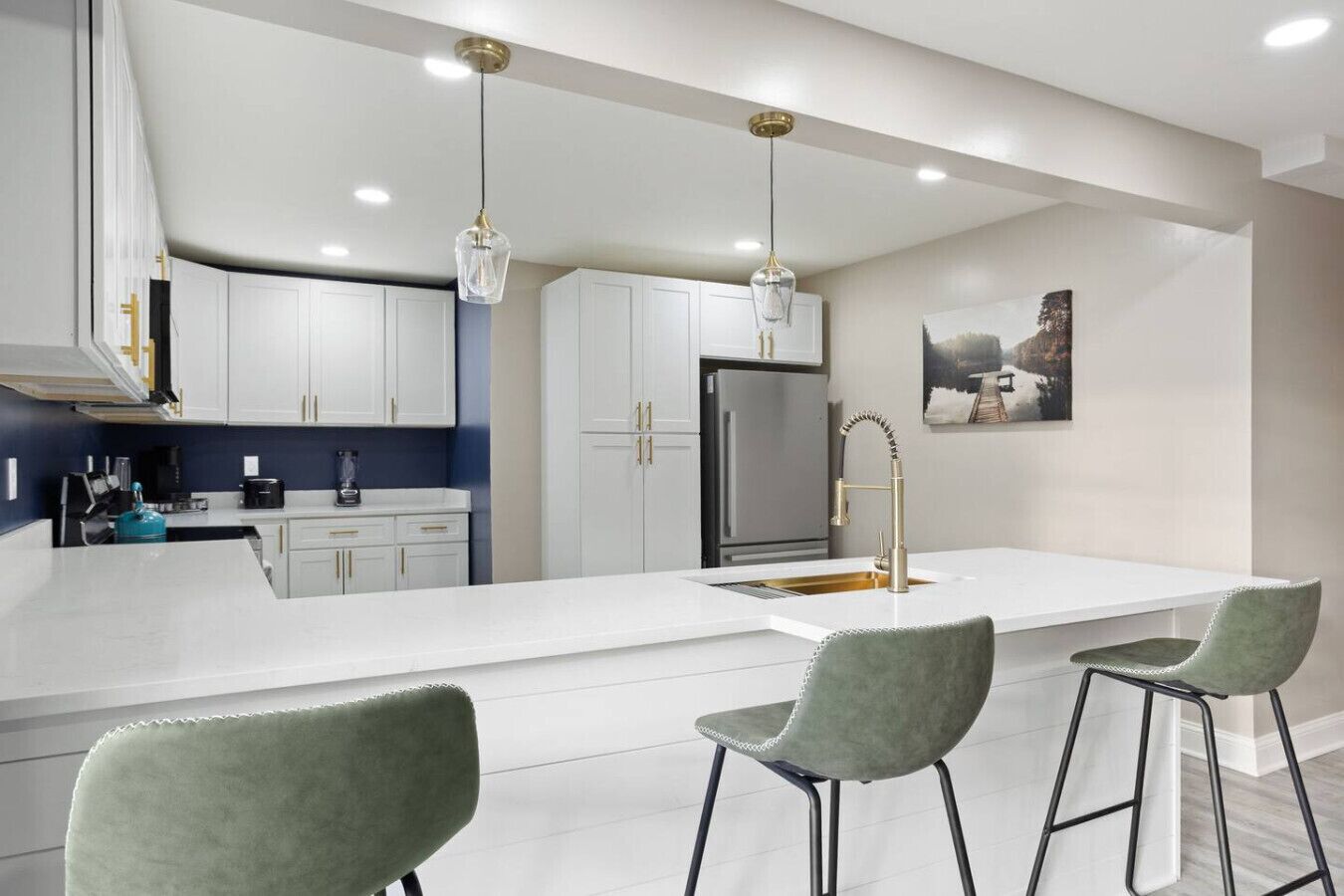 A modern kitchen with white cabinets, a large island, bar stools, and pendant lighting.