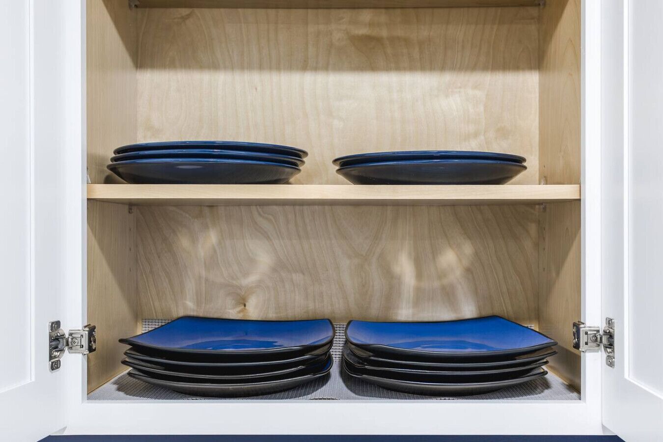 Un mueble bajo con dos estantes, cada uno con platos y servilletas azules dobladas.