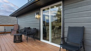 Une terrasse dotée de mobilier d’extérieur, notamment de chaises et d’une table, et une porte-fenêtre coulissante donnant sur un espace intérieur.