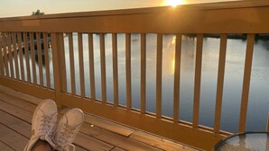 Eine Holzterrasse mit Geländer, von der aus sich ein Gewässer im Sonnenuntergang erstreckt.