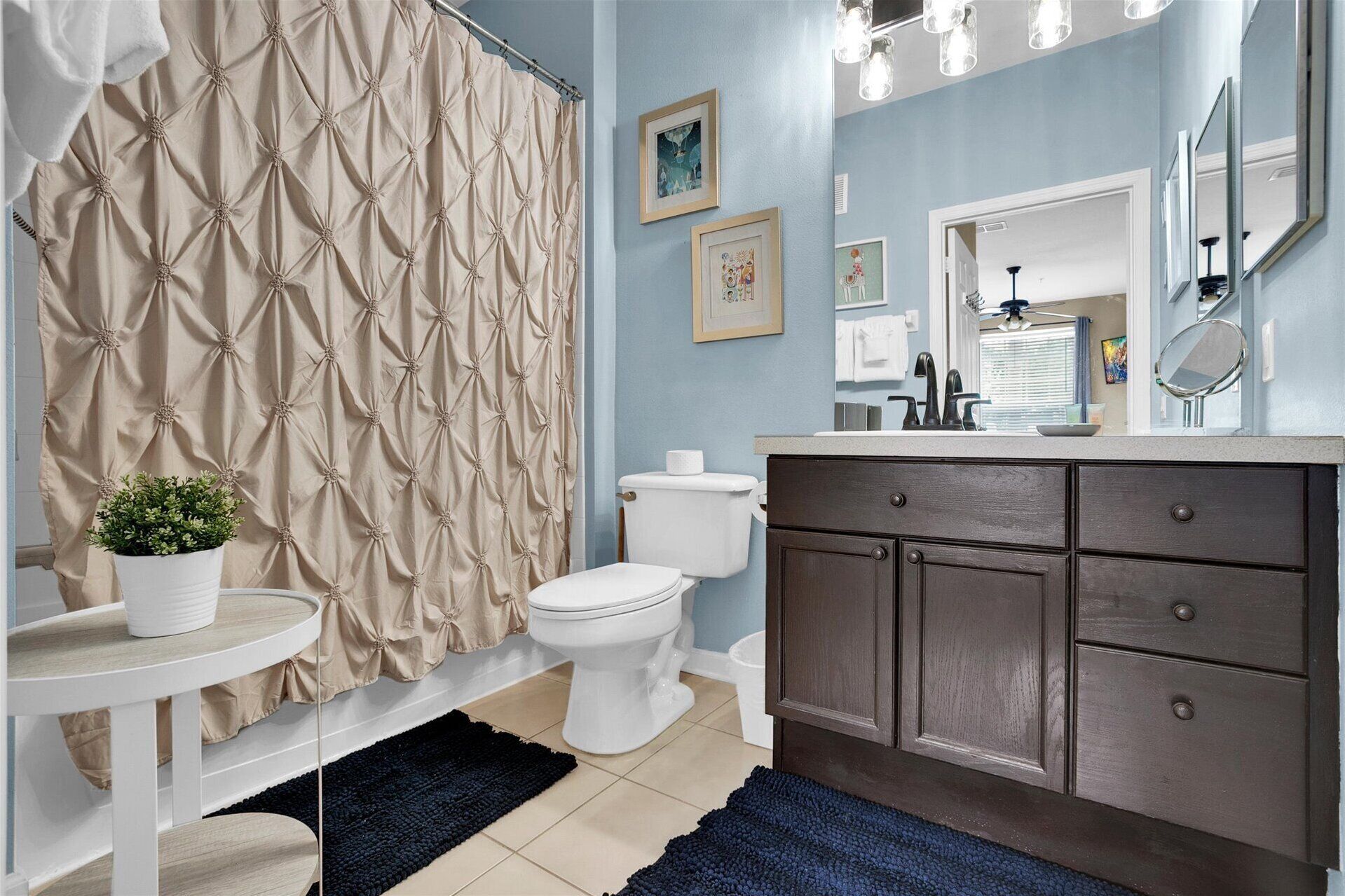 A bathroom with a beige curtain, a white toilet, a dark wooden vanity, and a small potted plant.