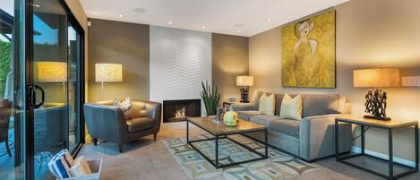 A modern living room with a sofa, coffee table, and lamps. There is a fireplace and a large painting on the wall.