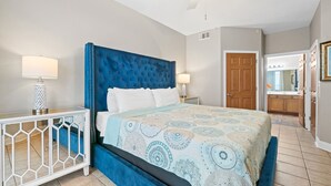 A bedroom with a large bed, a ceiling fan, and a nightstand with a lamp. - Sea Dunes 502 - Beach Oasis (Fort Walton Beach)