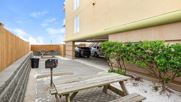 A courtyard with a picnic table, a wooden fence, a car, and a building with a beige exterior. - Sea Dunes 502 - Beach Oasis (Fort Walton Beach)
