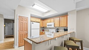 A kitchen with wooden cabinets, a white refrigerator, a microwave, a stove, and a granite countertop. - Sea Dunes 502 - Beach Oasis (Fort Walton Beach)
