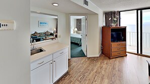 Quarto de hotel moderno com cozinha compacta, um espelho grande, um armário de madeira com televisão de tela plana e varanda com vista para o mar.