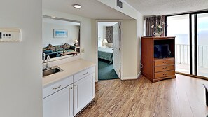 A modern hotel room with a kitchenette, a large mirror, a wooden cabinet with a flat-screen TV, and a balcony with a view of the ocean. - Sands Beach Club 1022 (Myrtle Beach)