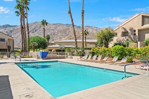 A swimming pool with lounge chairs and palm trees, surrounded by buildings and mountains. - Plaza Villas 615 (Palm Springs)
