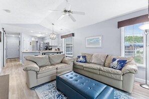 A modern living room with a beige sofa set, a blue ottoman, and a chandelier. - River Oaks 28G (Myrtle Beach)