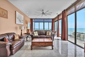 Ein großzügiges Wohnzimmer mit einem großen Fenster, das Meerblick bietet, einem Deckenventilator und Ledersofas mit Zierkissen.