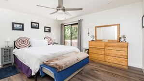 Un dormitorio con cama, cómoda, ventilador de techo y ventana con cortinas.