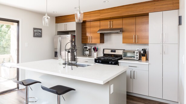 Una cocina moderna con muebles blancos, una isla central, electrodomésticos de acero inoxidable e iluminación colgante.
