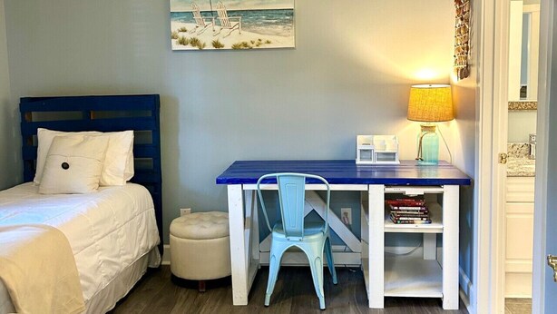 Ein Schlafzimmer mit Bett, Schreibtisch, Stuhl und einem Gemälde einer Strandansicht.
