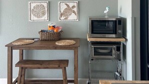 A kitchen with a wooden table, two wall art pieces, a microwave, and a small oven. - Sun & Sand @ the Landmark Resort (Myrtle Beach)