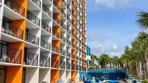 A hotel with a pool area, featuring a multi-level structure with balconies and a clear sky. - Sun & Sand @ the Landmark Resort (Myrtle Beach)