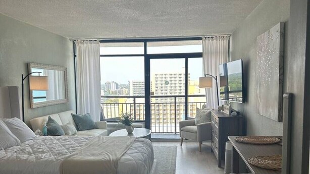 A hotel room with a large bed, a desk with a chair, a TV, and a balcony with a view of buildings. - Sun & Sand @ the Landmark Resort (Myrtle Beach)