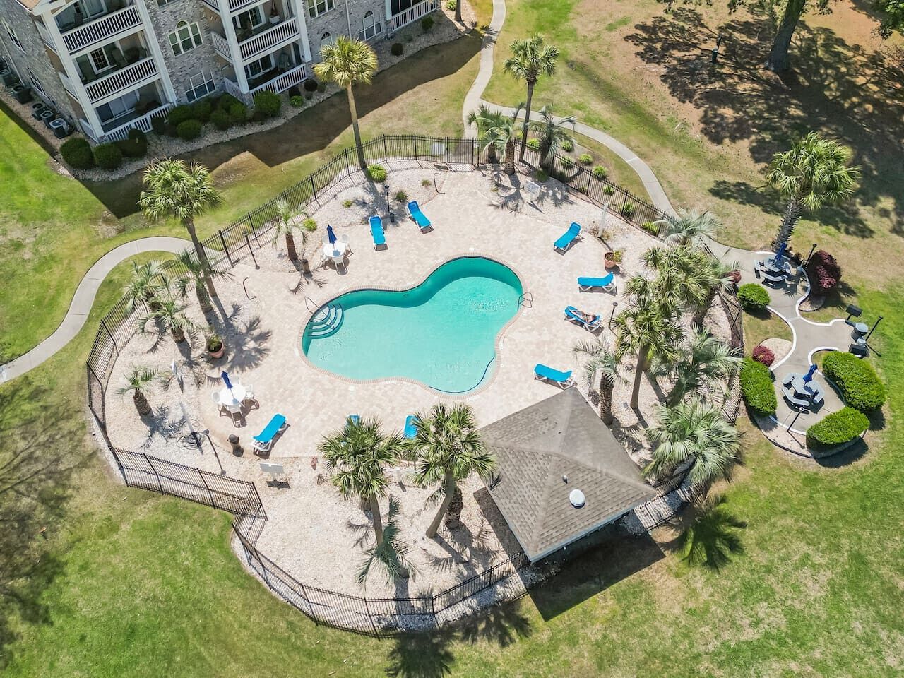 An aerial view of a hotel with a swimming pool surrounded by palm trees and sun loungers.