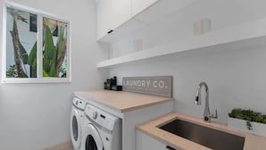 A compact laundry area with a washing machine, a sink, and a sign that reads "LAUNDRY CO. WASH, DRY, & FOLD". - Villa Granada by Rove Waterfront W/pool, Hot Tub (Miami)