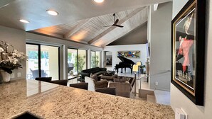 A spacious living area with a large window, a piano, and a ceiling fan. - Villa Cha Cha (Rancho Mirage)