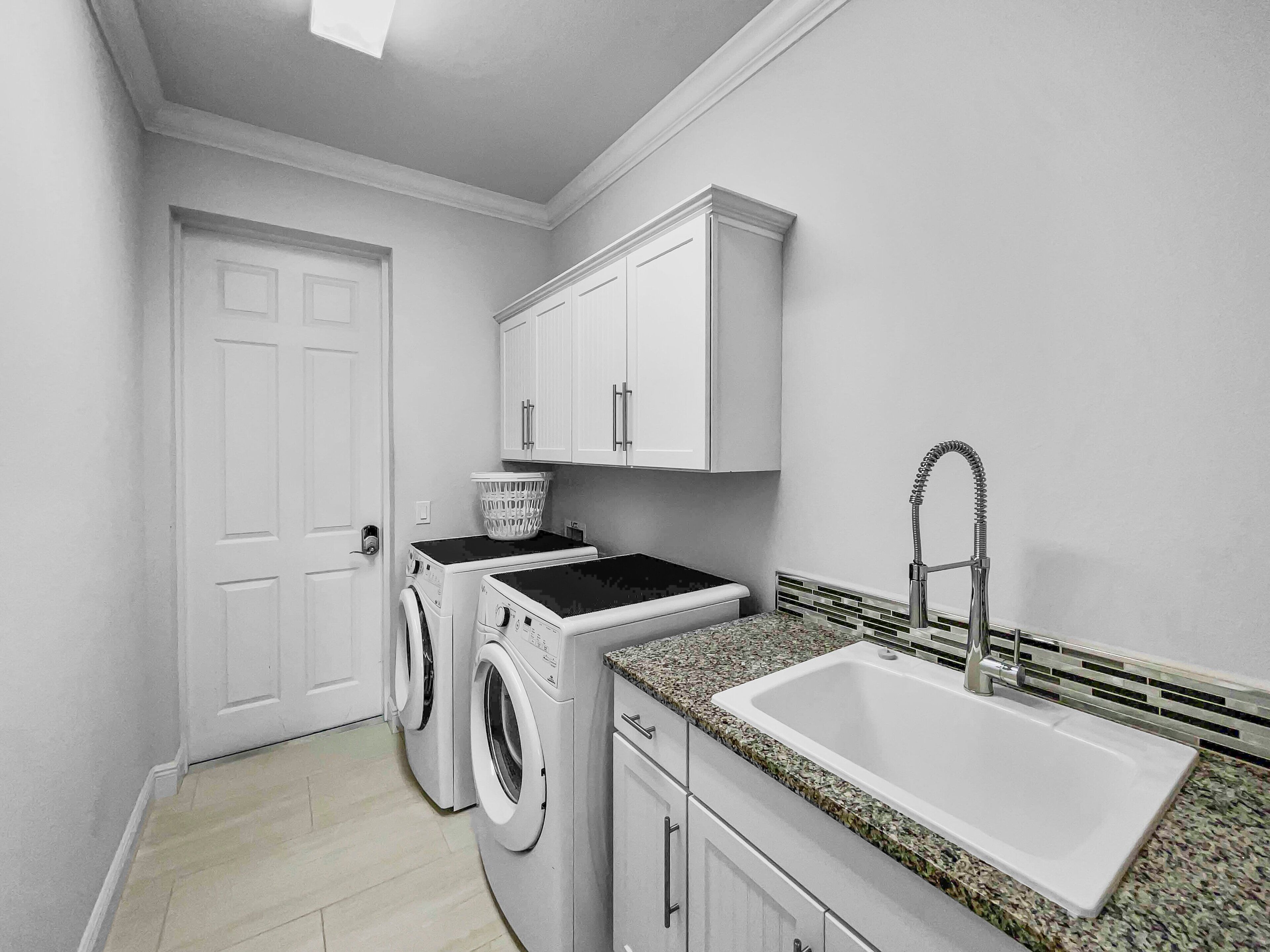 A laundry room with two washing machines, a sink, and a door.