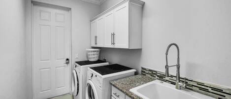 A laundry room with two washing machines, a sink, and a door.