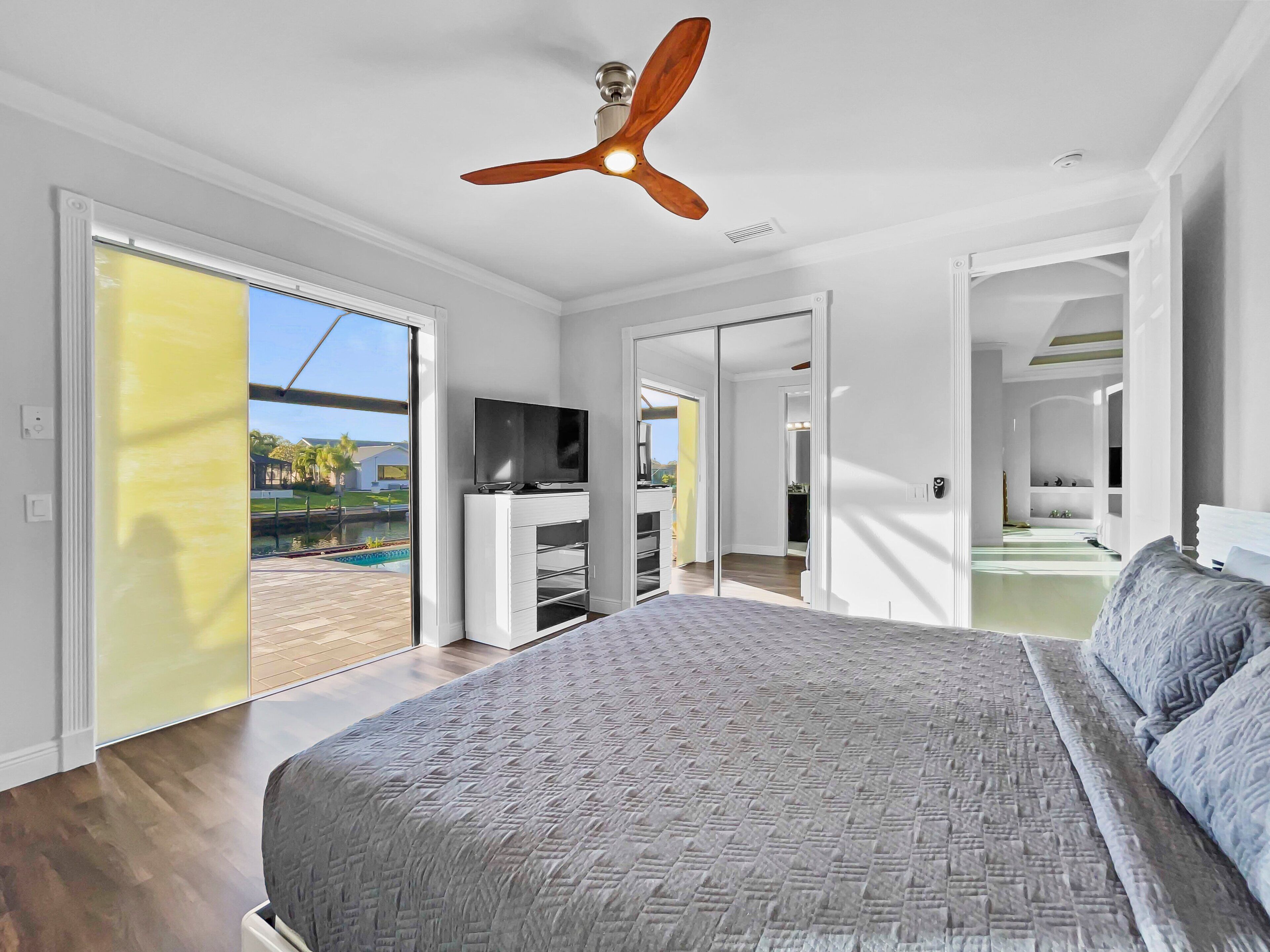 A bedroom with a large bed, a ceiling fan, a TV, and a sliding glass door leading to a pool.