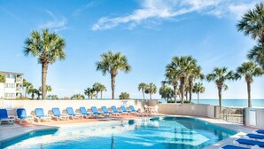Zona de piscina con sillas de descanso y palmeras, con vista a una masa de agua.