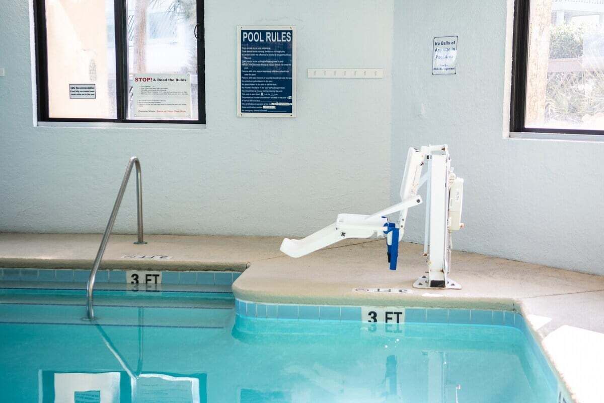 Una piscina con indicador de profundidad de 3 pies, un elevador de piscina y carteles que incluyen 'POOL RULES' y 'STOP! & Read the Rules'.