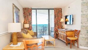 Habitación de hotel con balcón, sofá, mesa de comedor y televisor.