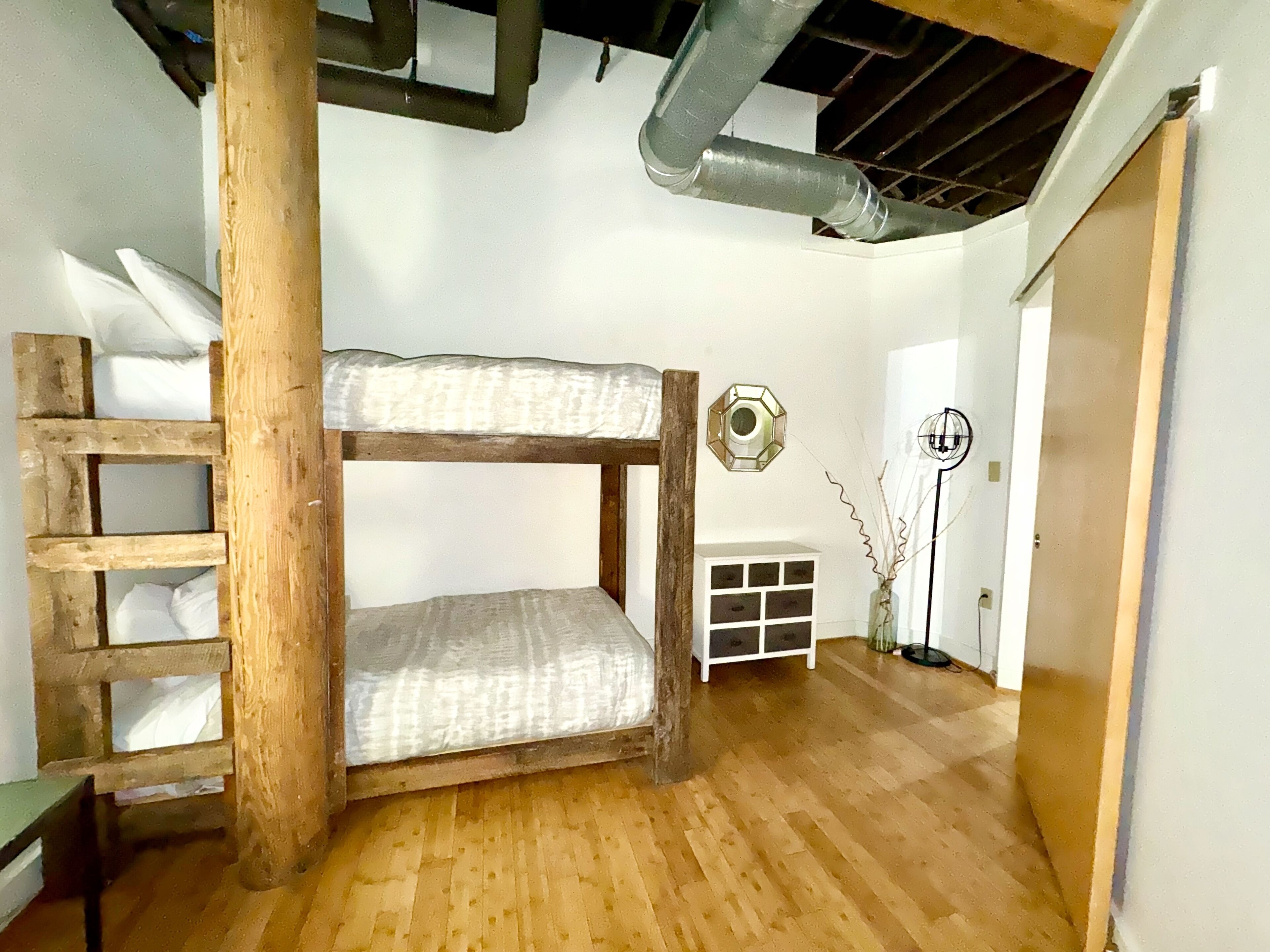 Una litera con escalera, un armario blanco, un espejo hexagonal decorativo y una lámpara de pie.