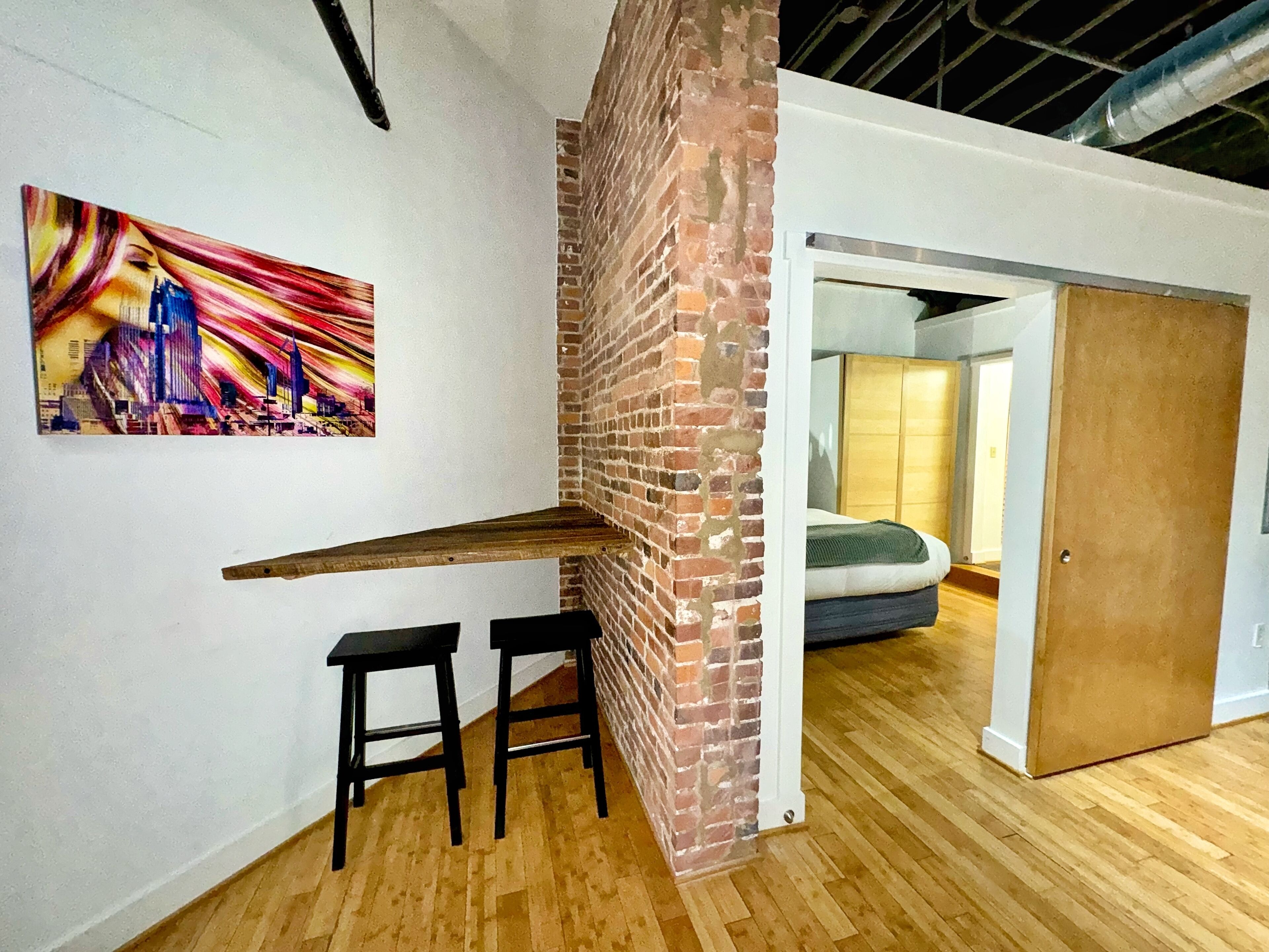 A modern interior with a brick accent wall, a wooden bench, and a colorful abstract painting.