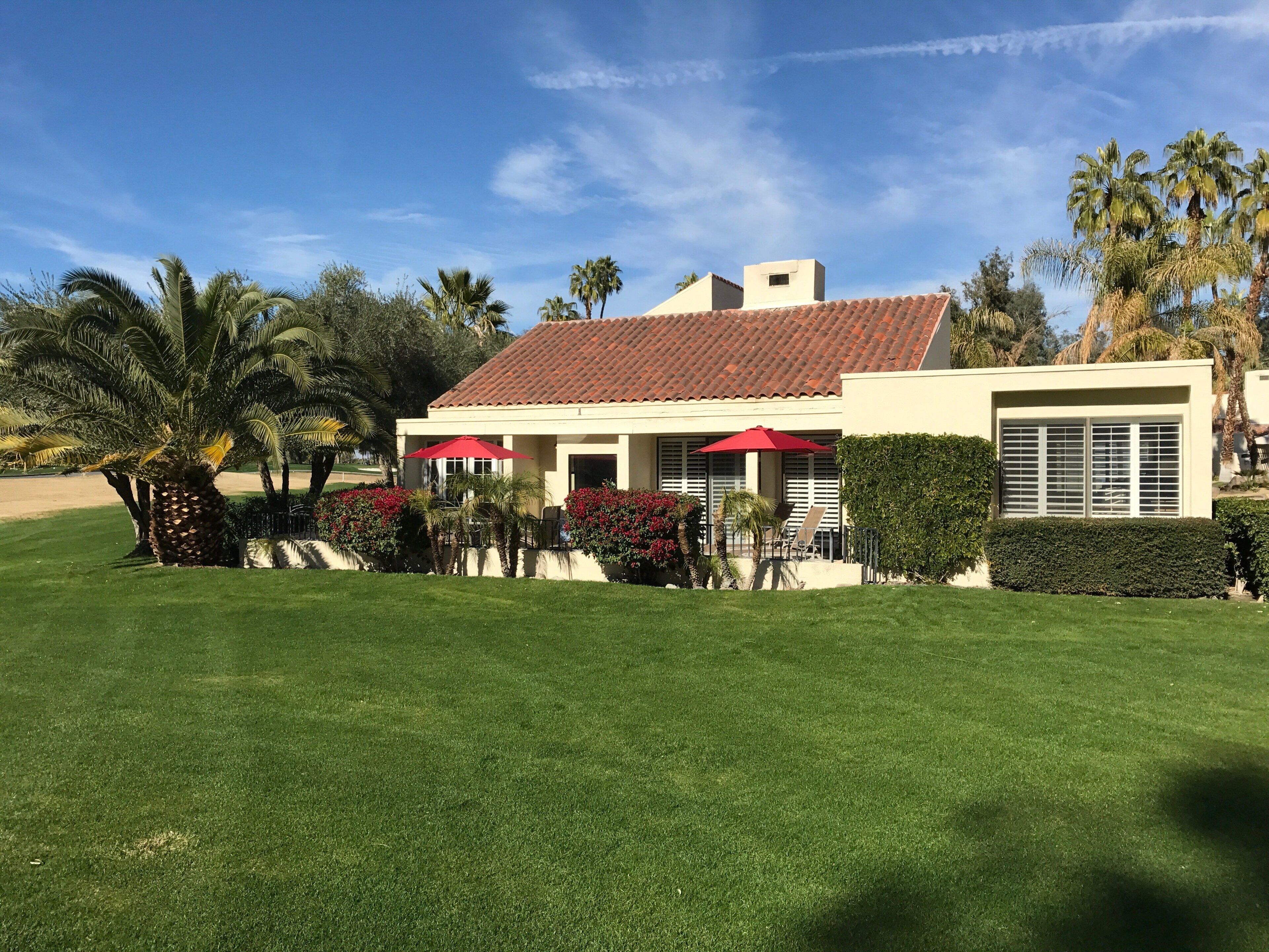 A modern building with a red-tiled roof, a covered patio with red umbrellas, and a well-maintained lawn.