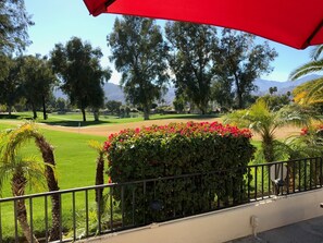 Une vue sur un terrain de golf, avec un parasol rouge, une végétation luxuriante et des montagnes au loin.