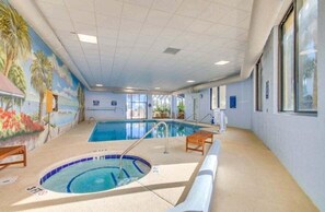 An indoor swimming pool with a mural on the wall, a lounge area, and a view of the outdoors through large windows. - Ocean Forest Plaza Unit 1412 (Myrtle Beach)