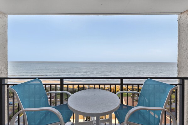 A balcony with a white table and blue chairs, overlooking a beach. - Ocean Forest Plaza Unit 1412 (Myrtle Beach)